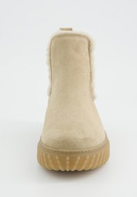 Béžová nubuková kotníková bota s umělou kožešinou uvnitř, polstrovaným límcem a texturovanou gumovou podešví. Design je minimalistický, bez viditelného kovového doplňku.