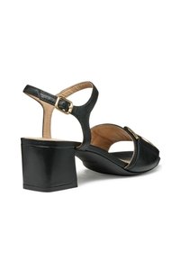 Zapato negro de piel tipo slingback con punta descubierta, detalles dorados y un tacón ancho. El interior presenta un forro suave beige.