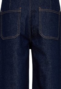 Vue arrière d'un jean en denim bleu foncé montrant deux poches arrière carrées avec des coutures orange et une couture centrale.