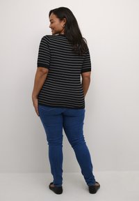 Top a righe nere con maniche corte, abbinato a jeans blu. Il top ha una silhouette aderente e righe bianche in contrasto. Scarpe nere basse.