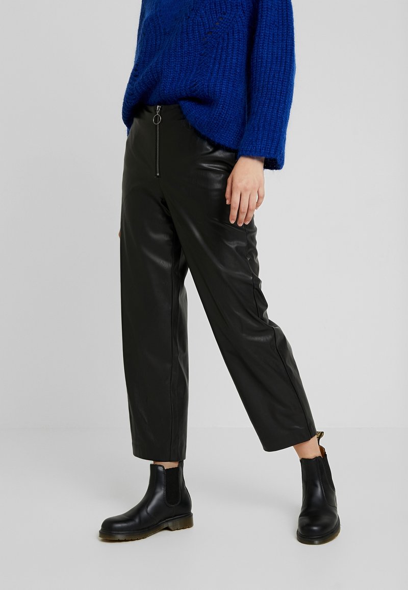 Czarne skórzane spodnie o luźnym kroju, z suwakiem z przodu i metalowymi detalami, zestawione z masywnymi czarnymi botkami za kostkę. Kobaltowy, dzianinowy sweter.