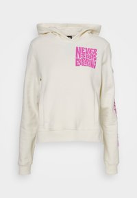 Sweat-shirt crème avec capuche, présentant un graphique carré en rose indiquant "NEVER STOP EXPLORING" et un texte supplémentaire en rose sur la manche.