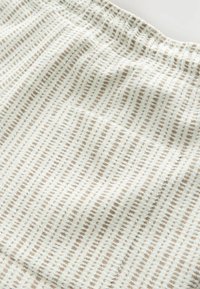 Gestructureerde stof in lichtcrème met een subtiel bruin rasterpatroon. Het materiaal oogt zacht, met een licht verhoogd oppervlak.