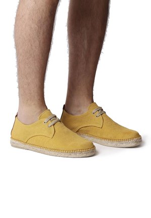 Espadrilles de lona amarillas con un acabado texturizado, que presentan una suela de yute trenzado y cordones de color marrón claro, diseño bajo.