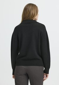 Juodas megztinis su plačiu apykaklės ir raštuotu apačiu, ilgomis rankovėmis, matomas iš nugaros. Lygus audinys, kasdieniškas siluetas.