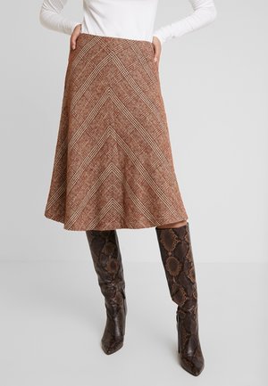 Woman wearing a brown plaid A-line skirt with pockets, paired with dark brown knee-high snakeskin boots and a white long-sleeve top.