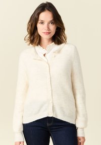 Kreemivärvi, ribakudumisega kardigan V-kaeluse, nupukinnituse ja pikkade varrukatega. Pehme, tekstureeritud kangas, millel on veidi üline sobivus.