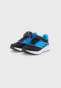 Μαύρα αθλητικά παπούτσια με μπλε λεπτομέρειες, υφασμάτινο επάνω μέρος, ιμάντα με βέλκρο και λευκή ελαστική σόλα. Διαθέτουν τρεις μπλε ρίγες στη πλευρά.