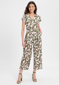 Olivgrüner Overall mit weißem Blattmuster, kurzen Ärmeln, V-Ausschnitt, Bindegürtel in der Taille, weitem Bein und Seitentaschen, kombiniert mit grünen High Heels.