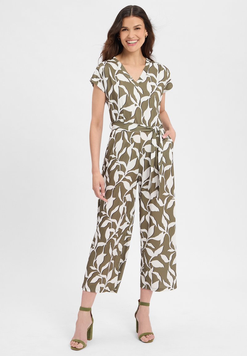 Olivgrüner Overall mit weißem Blattmuster, kurzen Ärmeln, V-Ausschnitt, Bindegürtel in der Taille, weitem Bein und Seitentaschen, kombiniert mit grünen High Heels.