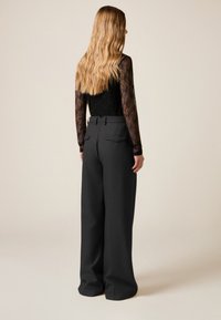 Czarna, koronkowa bluzka z długim rękawem w połączeniu z szarymi, szerokimi spodniami z wysokim stanem, posiadającymi dwie tylne kieszenie i szlufki na pasek.