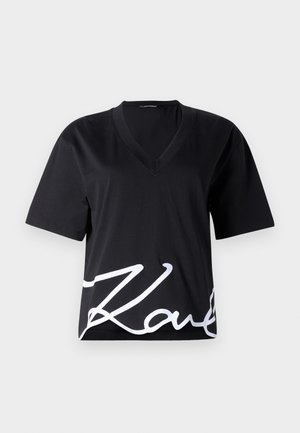 Camiseta negra de cuello en V hecha de una tela suave, con mangas cortas y una gran impresión blanca de firma en la parte inferior delantera.