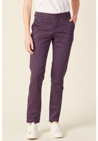 Slim-fit, patterned trousers in dark blue, red, and white. Features a buttoned waist, side pockets, and a smooth texture. Worn with white sneakers.