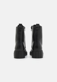 Botas de tobillo de cuero negro con suela acanalada, cremallera lateral y lengüeta de tirón, que presentan una textura suave y un diseño de punta redonda.