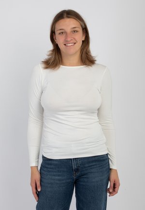 Top bianco a maniche lunghe realizzato in tessuto leggero, con scollatura rotonda e design aderente, abbinato a jeans in denim blu.