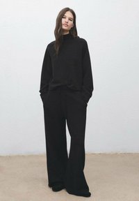 Sweatshirt noir surdimensionné avec col montant associé à un pantalon noir à jambes larges. Texture lisse, design minimaliste et sans motifs visibles.