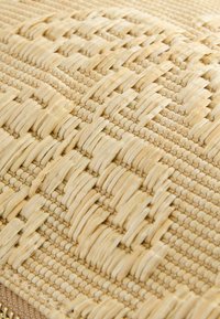 Gros plan sur un sac à main en paille tissée beige avec un motif carré texturé et un bord en cuir lisse.