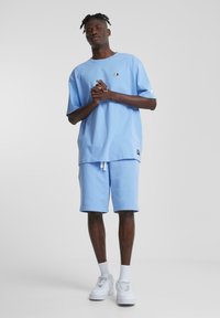 Light blue cotton t-shirt with short sleeves, paired with matching light blue shorts. Features a small logo and white drawstring.