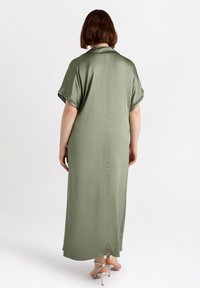 Satin olivgrön maxiklänning med avslappnad passform, korta ärmar, sidoick och en bakre sömdetalj, kombinerad med silvriga klackar.