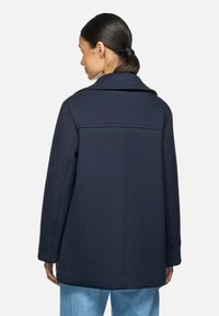 Cappotto blu navy con un design strutturato, caratterizzato da un ampio colletto e un taglio dritto. Tessuto liscio con dettagli minimi sul retro.