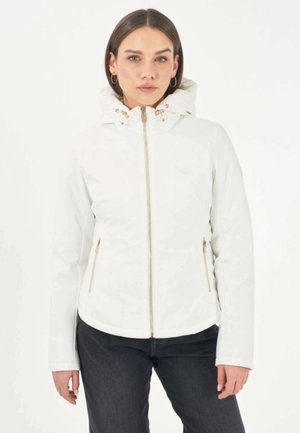 Donna che indossa una giacca bianca con cappuccio, zip frontale e tasche con cerniera, abbinata a pantaloni scuri, in piedi davanti a uno sfondo bianco.