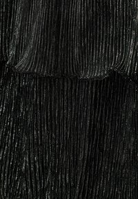 Čierna plisovaná tkanina so lesklými kovovými vláknami, vytvárajúca textúrovaný vzor. Hladké okraje s vrstveným dizajnom, ktorý pridáva dimenzie.