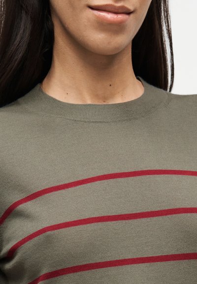 Πουλόβερ ελιάς με στρογγυλή λαιμόκοψη, διακοσμημένο με οριζόντιες κόκκινες ρίγες. Το ύφασμα φαίνεται λείο με πλεκτή υφή.