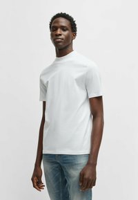 White short-sleeve t-shirt with a high neckline, made of smooth material. Worn with blue denim jeans, featuring a light wash and slight texture.
