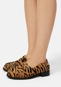 Tiger-striped loafers in tan and black, made of textured material. Features a low heel and soft upper with a rounded toe design.
