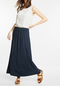 Bílá bezrukávová blůza s krajkovým zdobením spárovaná s volnou námořnickou maxi sukni. Pohodlné hnědé sandály dokončují celý outfit.