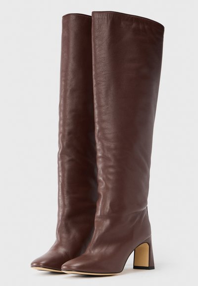 Brązowe, skórzane kozaki sięgające do kolan, o gładkiej fakturze i spiczastym nosku, z zwężanym obcasem typu blok zapewniającym stabilność.