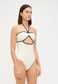 Jednodílné plavky v off-white barvě s černými akcenty, s vyřezávaným designem, zavazováním za krk a strukturovanou tkaninou.