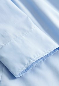 Tela azul claro con costuras y detalles de las uniones visibles, doblada para mostrar la textura estratificada del textil y un dobladillo limpio.