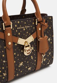Brun och mörk mönstrad handväska med guldfärgade stjärndekorationer, Michael Kors-logotyp och detaljer i form av guldlås och nyckel på framsidan.
