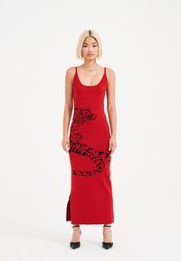 Ein Model mit einem eleganten Bob trägt ein figurbetontes rotes Kleid mit einem schwarzen Tigerdesign. Sie steht selbstbewusst in schwarzen High Heels.