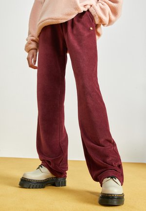 Pantalons en velours côtelé bordeaux avec une coupe décontractée, présentant une texture côtelée et un logo brodé près de la poche, accompagnés de chaussures à plateforme crème.