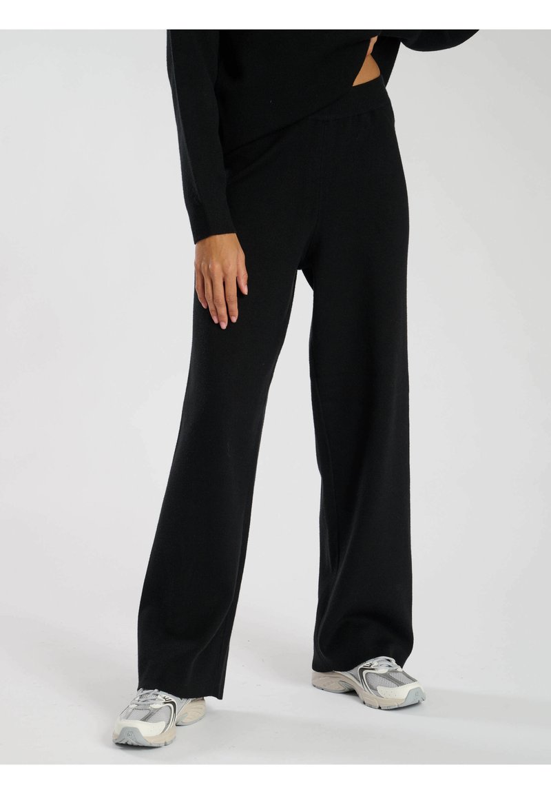 Svarta vida byxor i mjukt tyg med resårmidja. Matchas med ljusgrå sneakers för en avslappnad look.