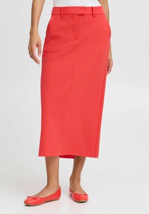 Jupe rouge de longueur genou en tissu lisse, présentant une taille ajustée et une coupe droite. Associée à des chaussures plates rouges assorties.