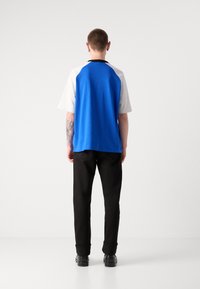 Short-sleeve shirt with a blue back and gray front, paired with black pants. The shirt features a round neckline and is relaxed-fit.