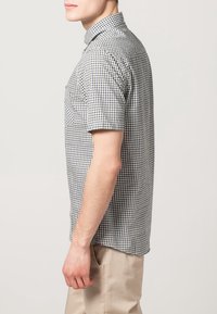 Camicia a maniche corte a quadretti in bianco e nero, con colletto standard e taglio dritto. Il tessuto appare leggero e traspirante.
