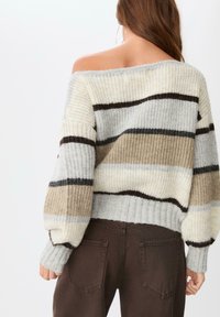 Pleteni pulover s dizajnom bez ramena, svijetlosivi, bež i tamnosmeđi prugasti uzorak, s rebrastim manžetama i rubom. Uparen s smeškim trapericama.