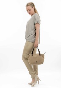 Borsa tote beige con manici tartarugati, forma arrotondata e logo frontale. Indossata con pantaloni fitted beige chiaro e tacchi alti color crema.