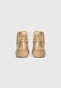 Metalické zlaté členkové topánky s hladkou textúrou, s detailom zipsu a robustnou, textúrovanou béžovou podrážkou. Navrhnuté pre pohodlie a trvanlivosť.