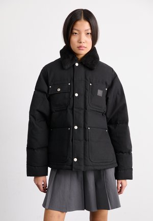 Veste en duvet noire avec un col en fausse fourrure, plusieurs poches frontales et des fermetures à boutons-pression, présentant une surface extérieure lisse et texturée.