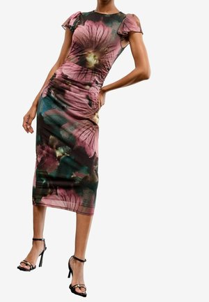 Femme portant une robe midi cintrée avec un grand imprimé floral rose et vert et des manches volantes, associée à des sandales à talons noires.