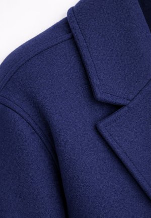 Col droit en laine bleu foncé et épaule avec couture visible et texture lisse sur fond blanc.