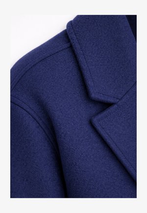 Mørkeblå uldfrakk krave og skulder med synlige sømme og glat tekstur på hvid baggrund.