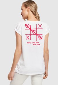 Hvit T-skjorte med kort erm med et rødt terningspill-design med hjerter og teksten "TRE PÅ RAD IKKE DIN..." på baksiden.