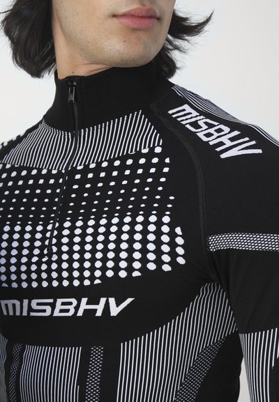 Crni zip-up top dugih rukava s kombinacijom bijelih točkastih i prugastih uzoraka, s imenom branda "MISBHV" istaknuto prikazanim.