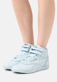 Ljusblå höga sneakers i slätt läder med perforerade detaljer, två justerbara remmar och en vadderad krage.